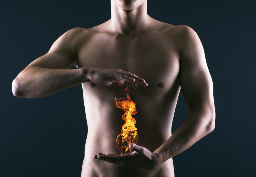 A naked man appears to be holding a flame of fire in front of his stomach to show that he is suffering from heartburn.