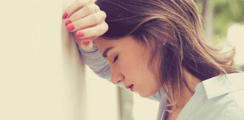 A young woman with her eyes closed is leaning her head against her hand that is touching the wall.
