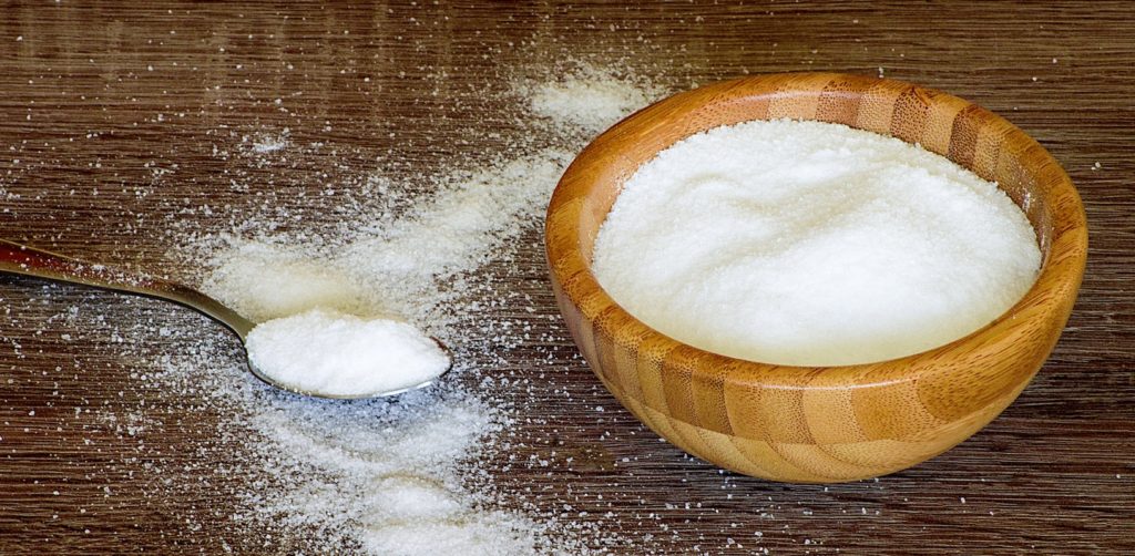 Salt in a wooden bowl, next to it is salt on a wooden spoon.