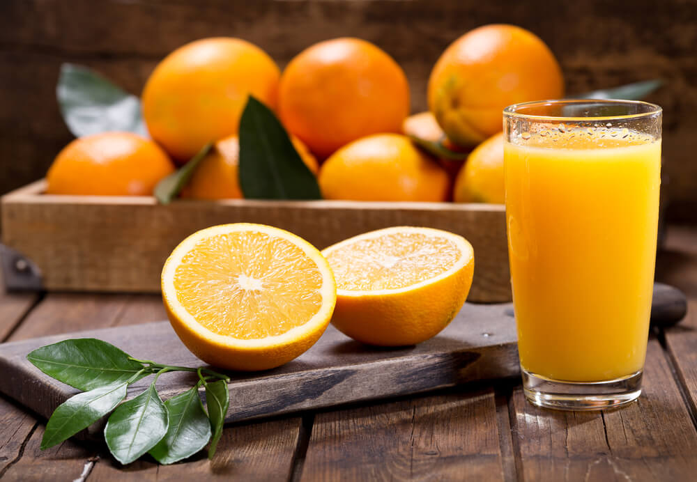 Frisch gepresster natürlicher Orangensaft in einem Glas, daneben Orangen auf einem Holzbrett.