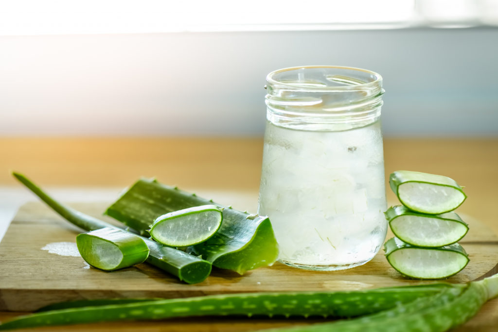 A fresh leaf of aloe vera and a glass of aloe vera juice on a wooden board.