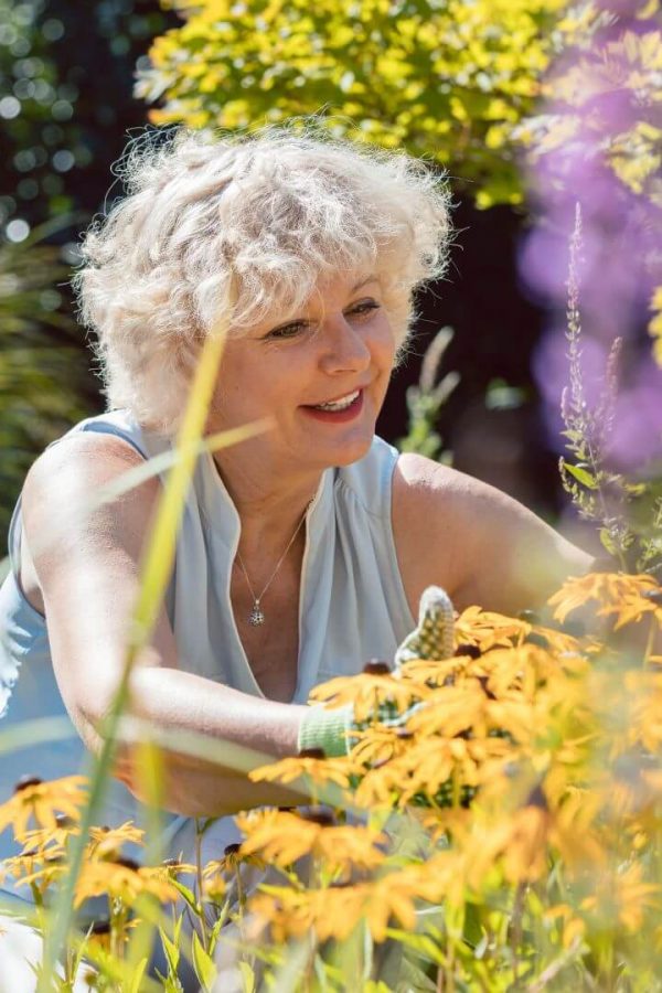 Starija žena sređuje cvijeće u svom vrtu.