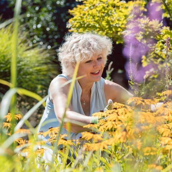 Eine ältere Frau arrangiert Blumen in ihrem Garten.