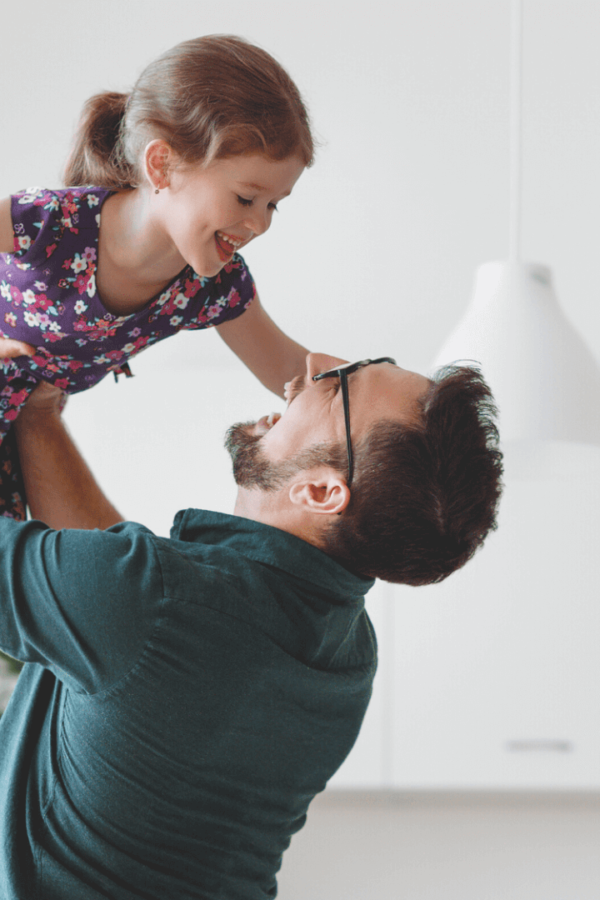 Un padre felice solleva la figlia in alto per aria, mentre ridono forte entrambi.