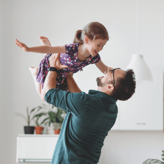 A happy dad is lifting his daughter high up in the air. They are both laughing hard.