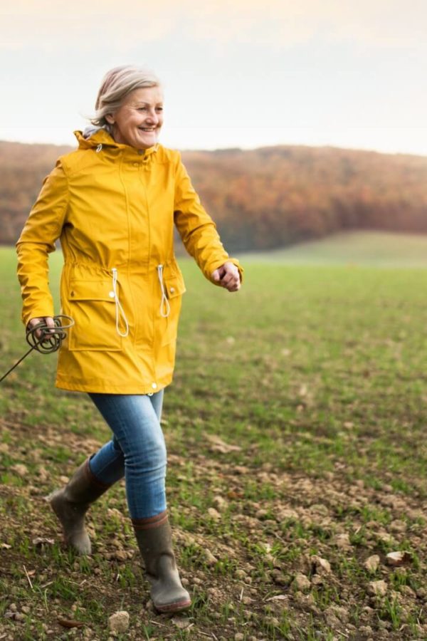 Nasmejana gospa v rumenem dežnem plašču se sprehaja s psom.