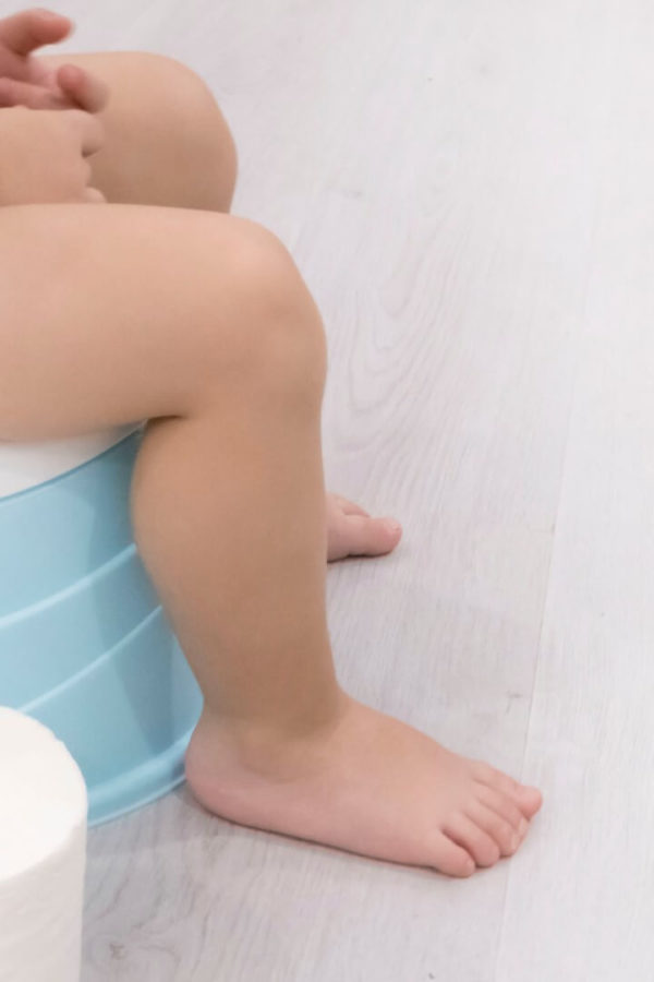 A little child is sitting on a blue potty and there is a toilet paper roll next to her.