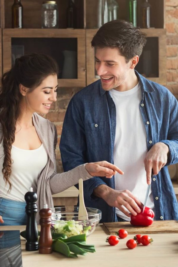 Una coppia giovane e felice prepara insieme il pranzo in cucina.