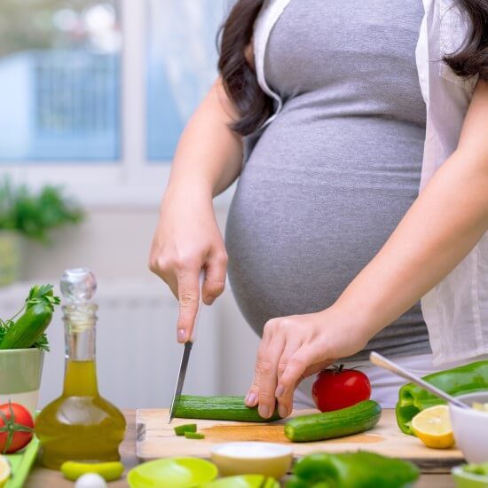 A pregnant woman is cutting vegetables for healthy lunch.