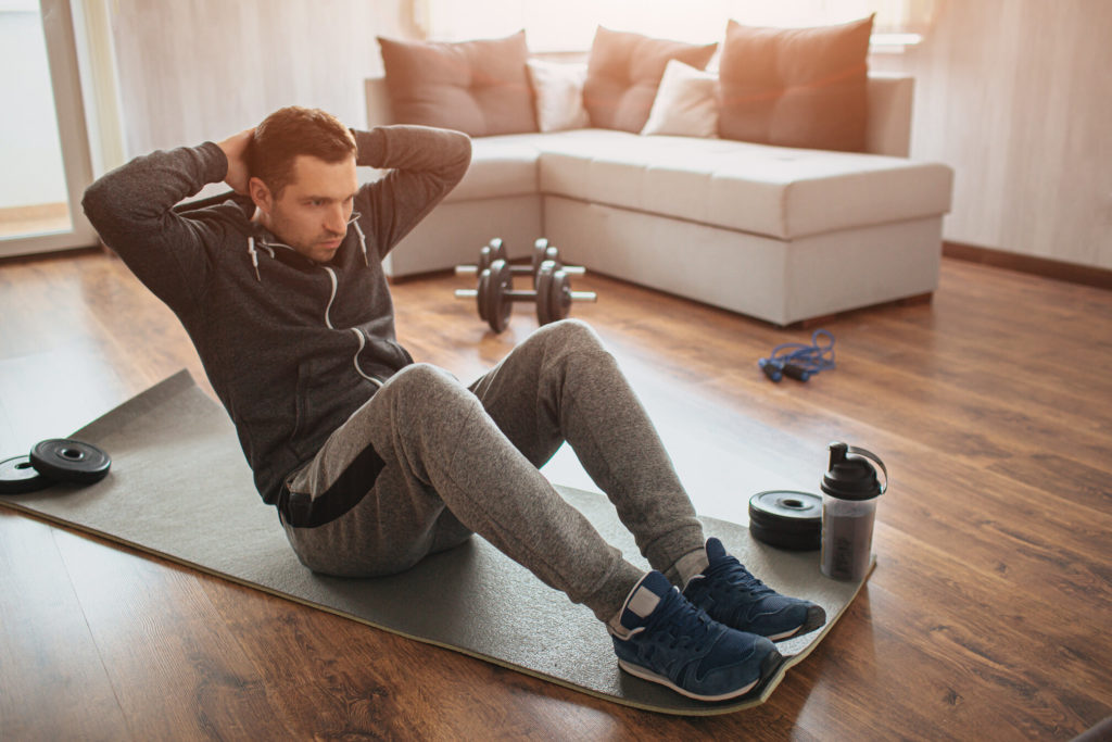 A young and fit man is doing stomach exercises on a soft floor mat at his home.