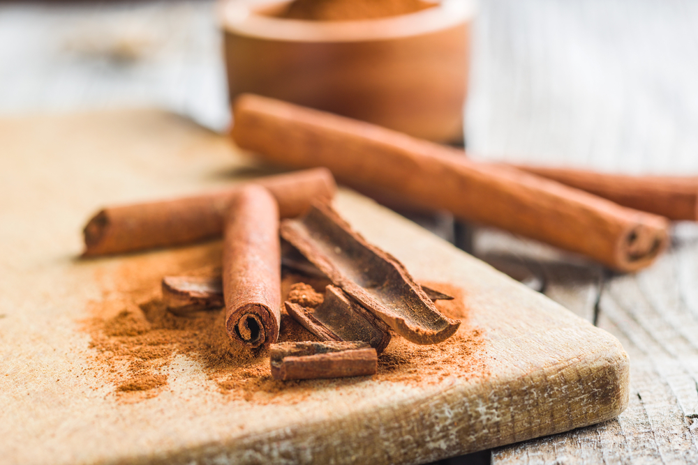 Rametti di cannella e cannella in polvere su un vecchio tagliere di legno.