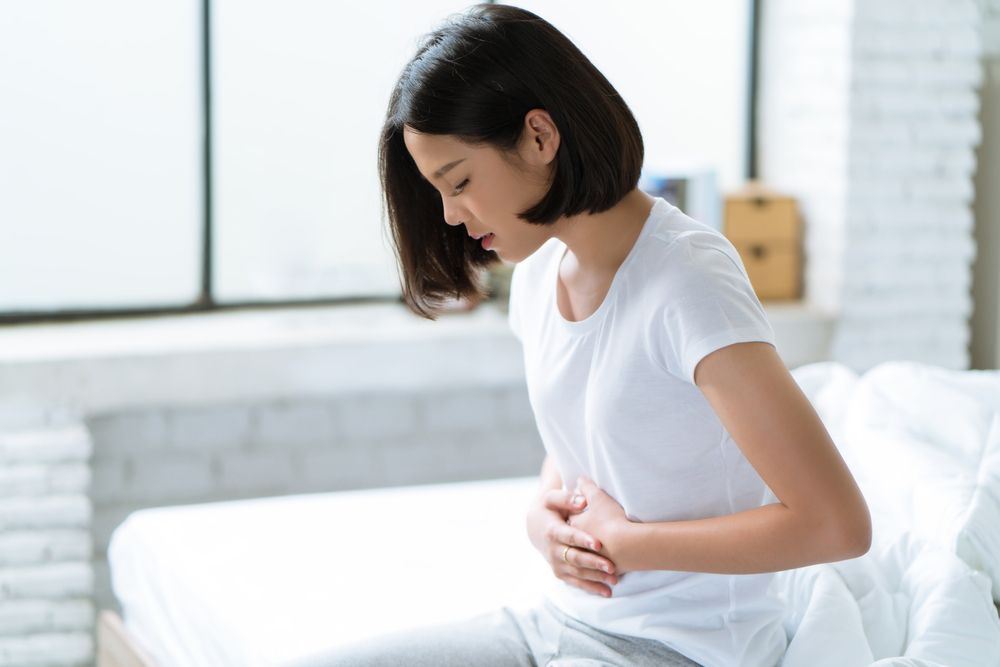A woman is clutching her stomach that hurts her due to constipation.