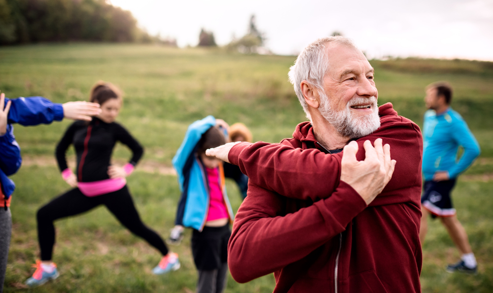 An older man is exercising with a group in a natural environment.