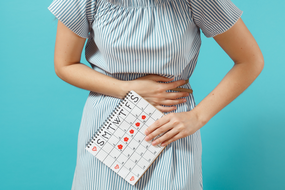 A woman holds on to her belly because she is bloated during period and holds a menstrual calendar in her hand.