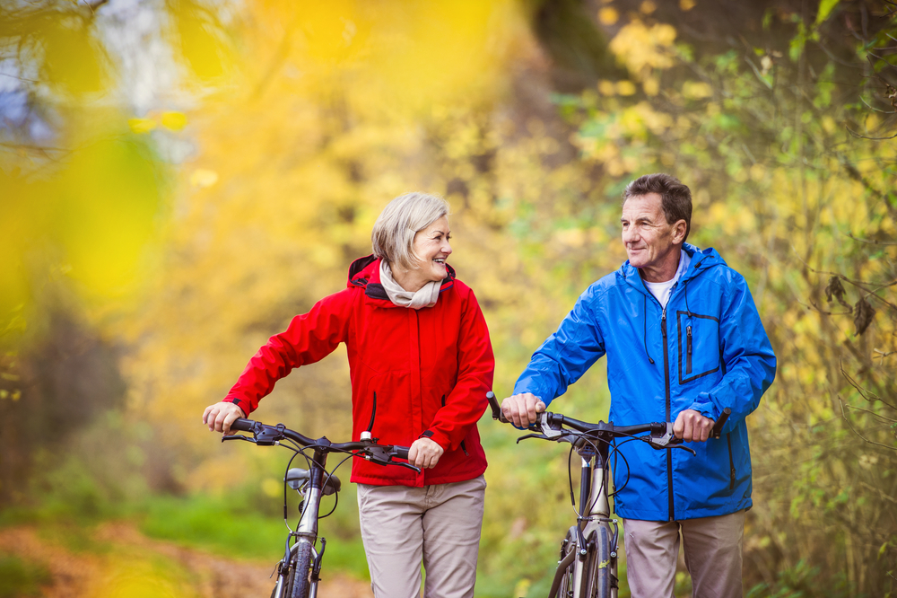 Aktivni starejši par na sprehodu s kolesom v jesenski naravi.