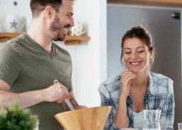 Nasmejana mož in žena skupaj pripravljata zdravo kosilo.